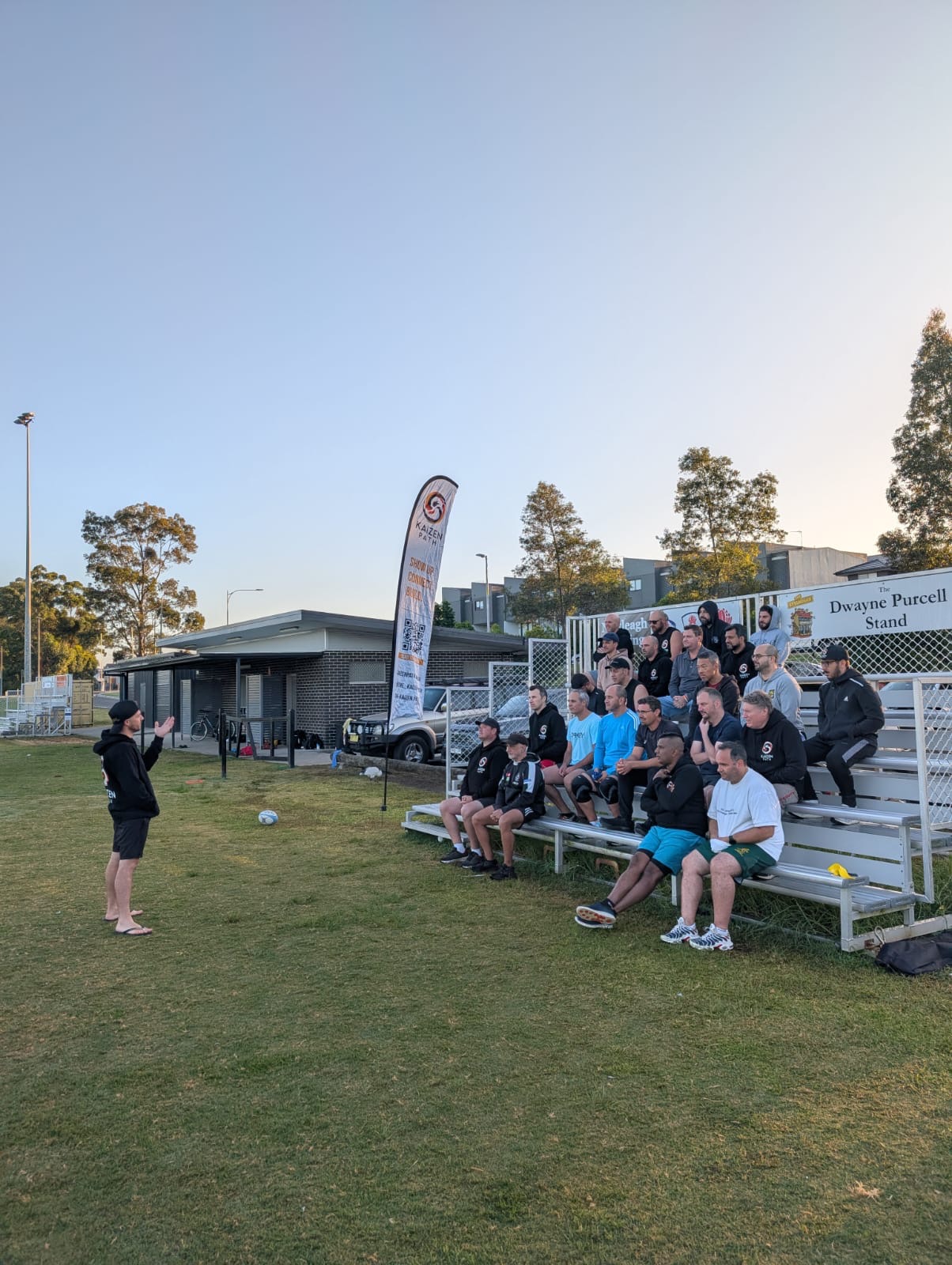 Aaron talking to the Kaizen Path lads seated together on outdoor grandstand benches