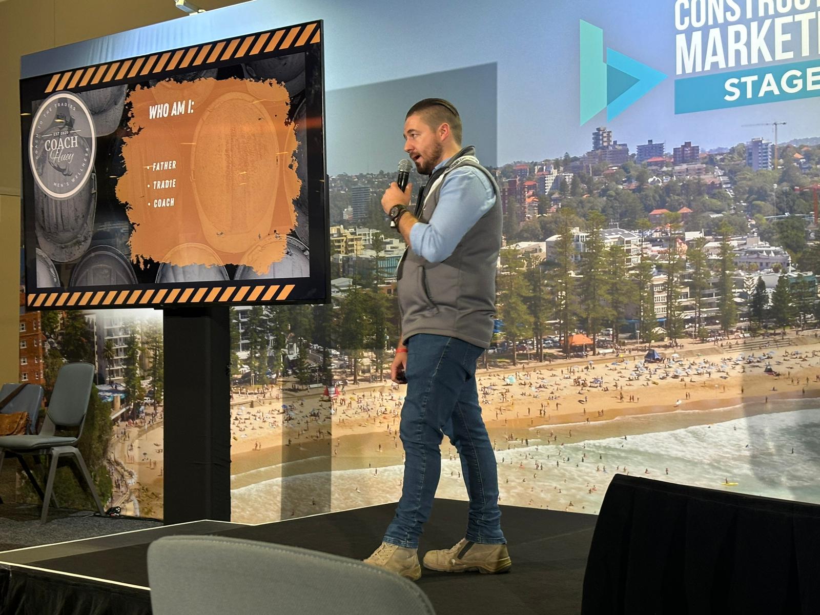 Aaron delivering a presentation on stage with a handheld microphone